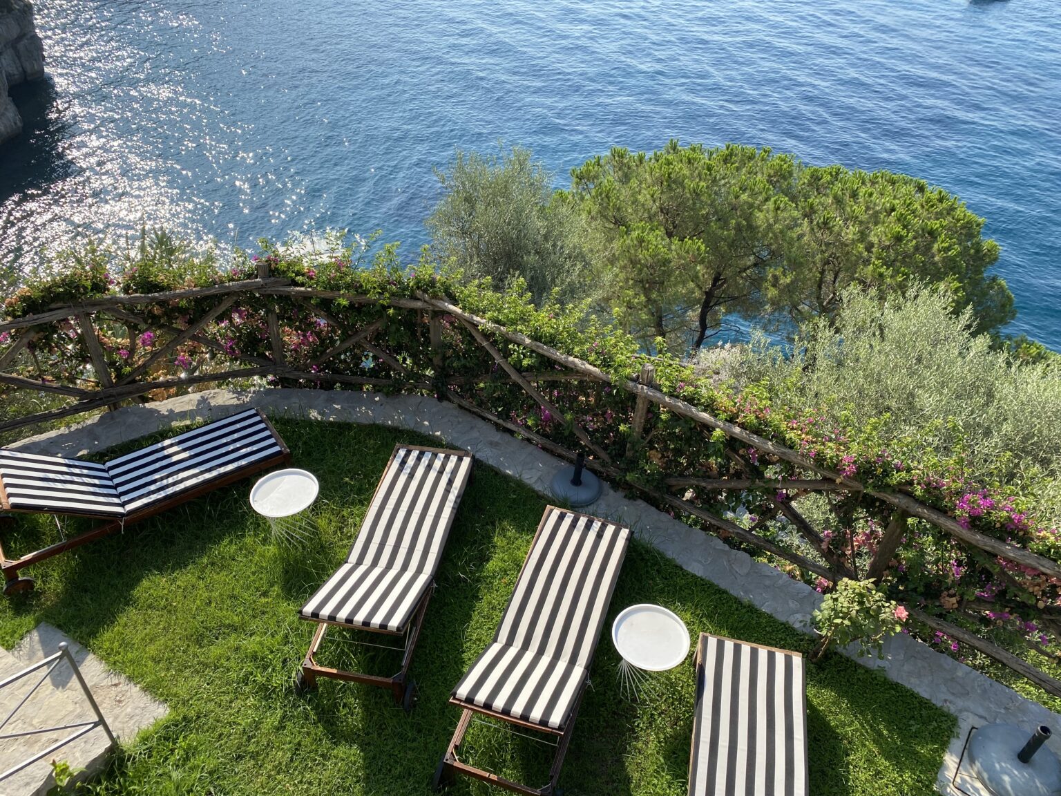 Luxury villas for rent in Italy featuring a scenic terrace with sun loungers overlooking the serene blue waters and lush greenery. Ideal for a relaxing getaway. | Only on SopranoVillas