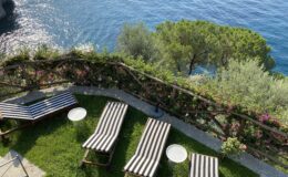 Luxury villas for rent in Italy featuring a scenic terrace with sun loungers overlooking the serene blue waters and lush greenery. Ideal for a relaxing getaway.
