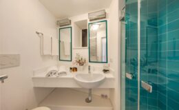 Modern bathroom featuring a sleek design with a glass shower, minimalist sink, and stylish mirrors. The turquoise tiles add a vibrant touch, while the decor includes subtle floral accents for a fresh look.