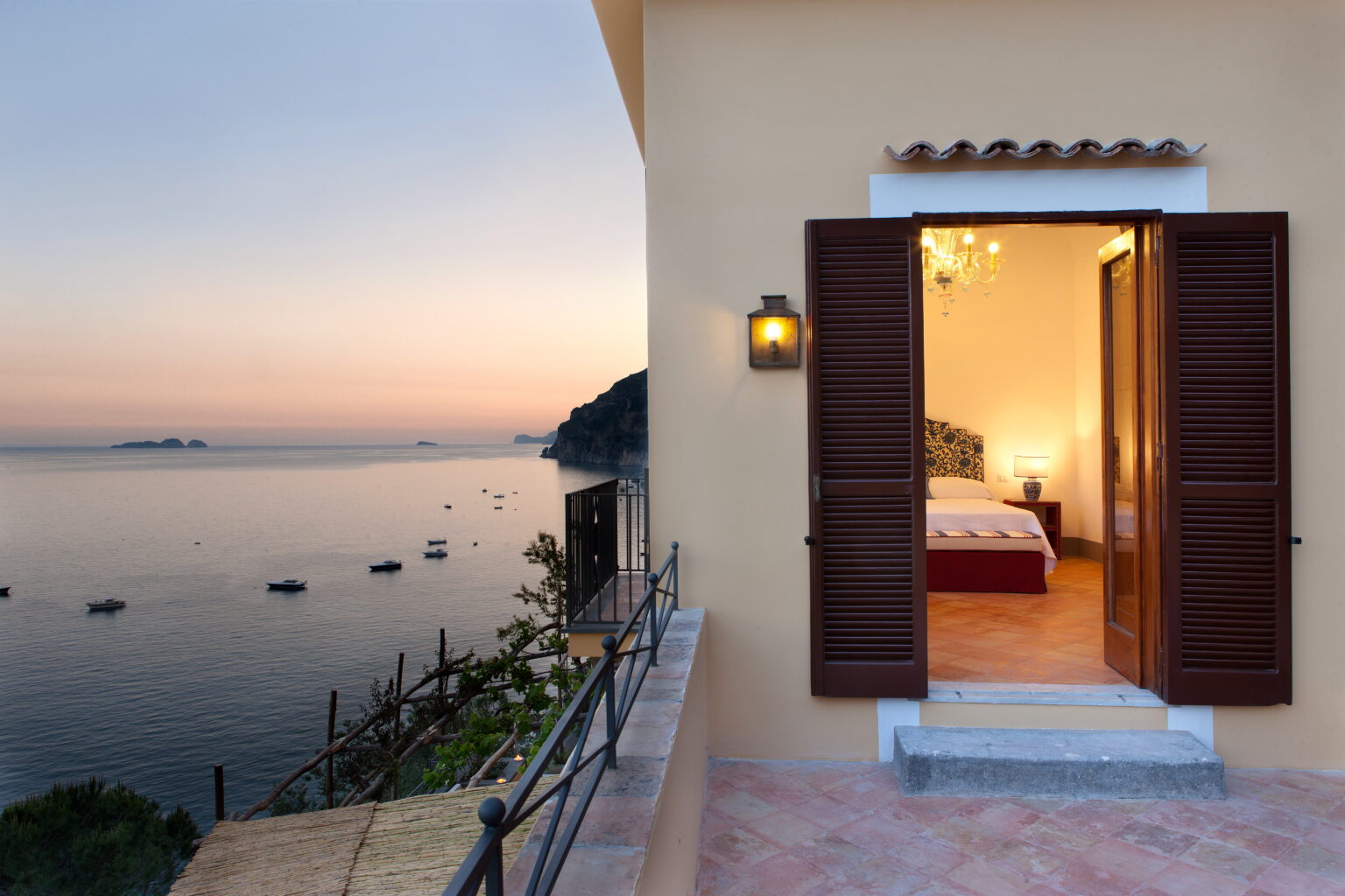 Luxury villa for rent in Italy featuring a stunning sunset view from the terrace, with open shutters revealing a beautifully decorated bedroom. Ideal for a serene getaway by the coast. | Only on SopranoVillas