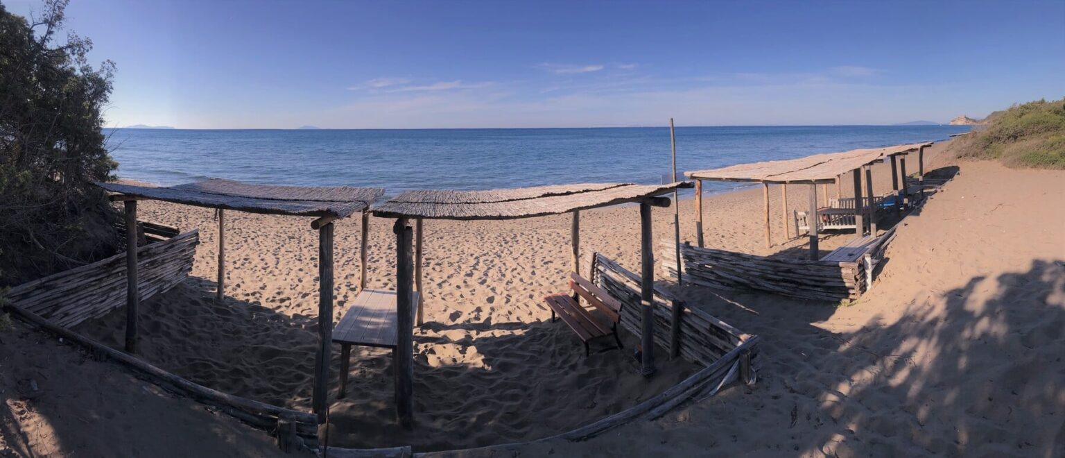 Scenic view of a sandy beach with wooden structures providing shade, overlooking calm blue waters and a clear sky. Ideal for relaxation and beach activities. | Only on SopranoVillas