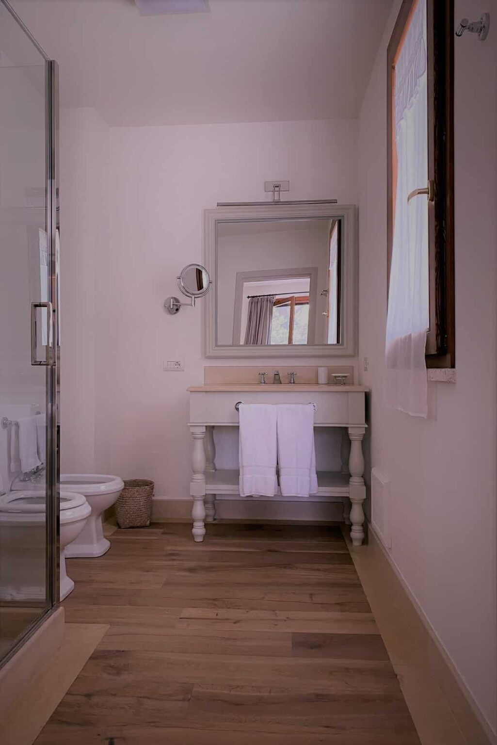 Modern bathroom interior featuring a stylish vanity with a large mirror, neatly arranged towels, and a glass shower enclosure. The decor is minimalistic with soft lighting and a clean aesthetic. | Only on SopranoVillas