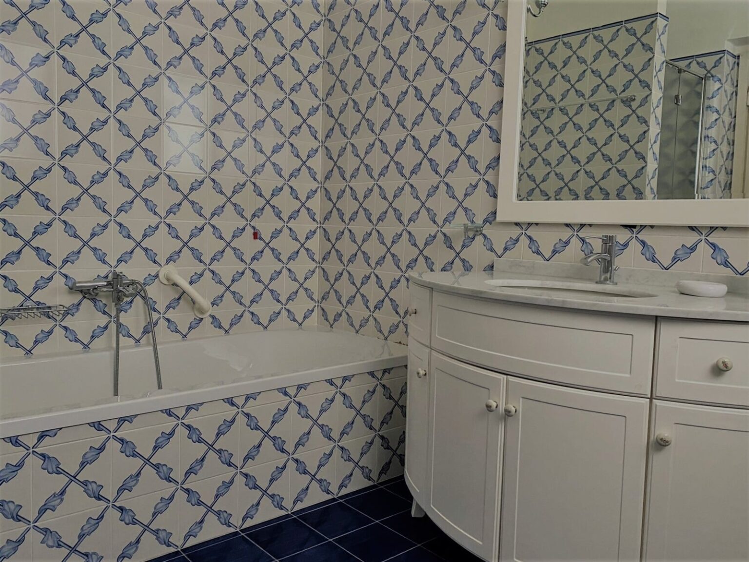 Bright and stylish bathroom featuring blue and white patterned tiles, a modern bathtub, a sleek white vanity with a mirror, and ample natural light. Ideal for home renovation inspiration. | Only on SopranoVillas