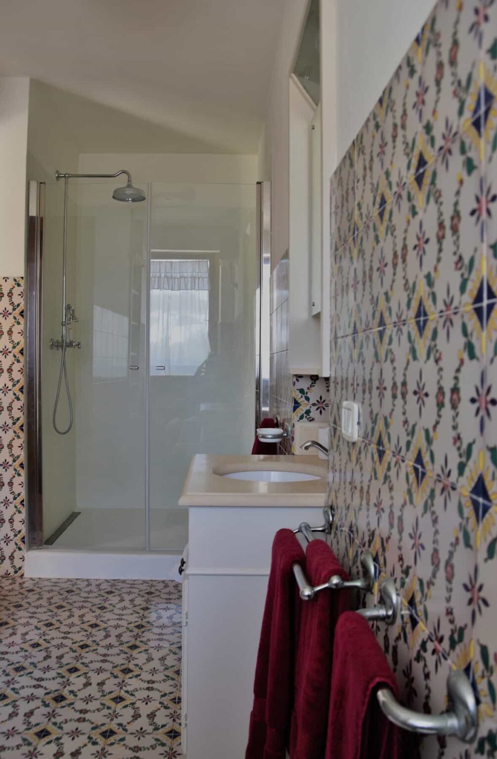 Modern bathroom featuring a glass shower enclosure, a sleek sink with a countertop, and decorative patterned tiles on the walls, creating a stylish and functional space. | Only on SopranoVillas