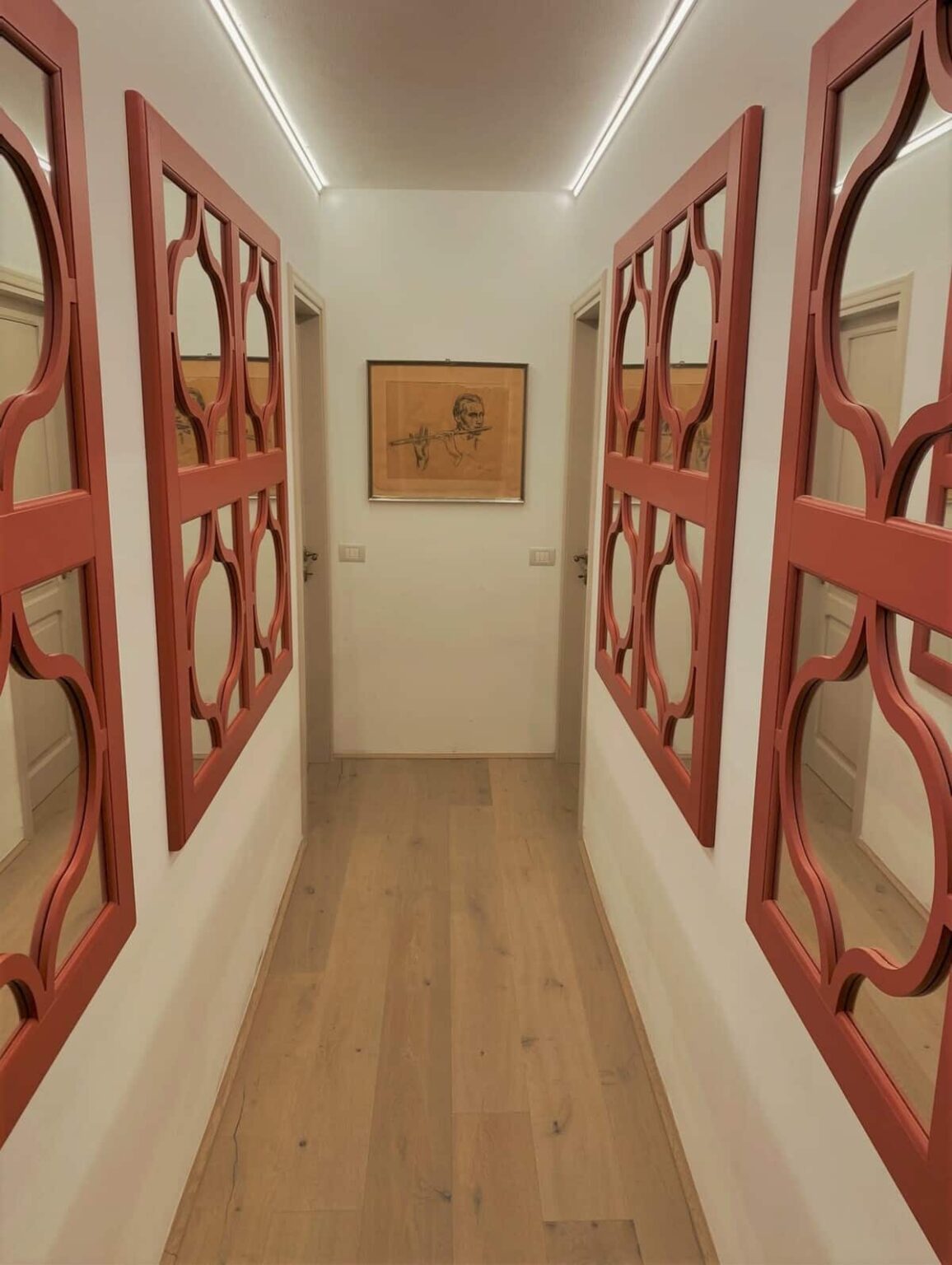 Interior view of a stylish hallway featuring decorative red wall panels and a framed artwork, with wooden flooring and soft lighting. | Only on SopranoVillas