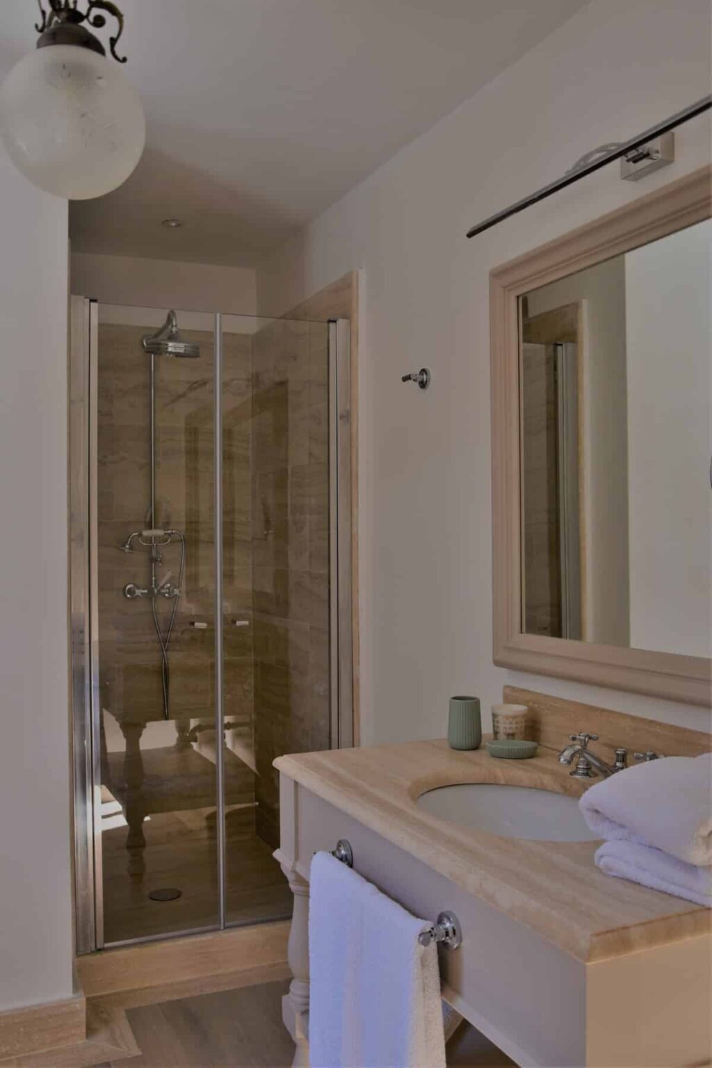 Modern bathroom featuring a glass shower enclosure, neutral-toned tiled walls, a wooden vanity with a mirror, and minimalist decor. | Only on SopranoVillas