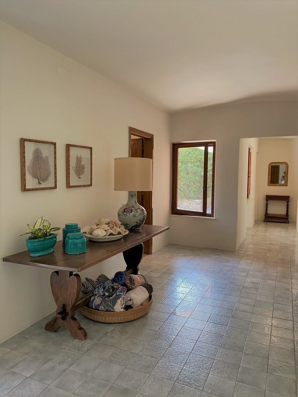 Bright and inviting hallway featuring a console table with decorative items, including seashells and plants, framed artwork on the walls, and natural light coming through a window. The space has a modern, minimalist design with warm tones and a serene atmosphere. | Only on SopranoVillas