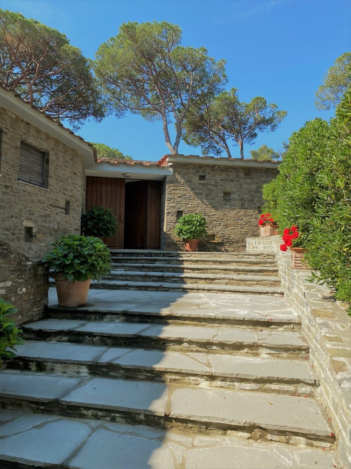 Stone staircase leading to wooden doors, surrounded by lush greenery and potted flowers, creating a welcoming entrance to a rustic home. | Only on SopranoVillas