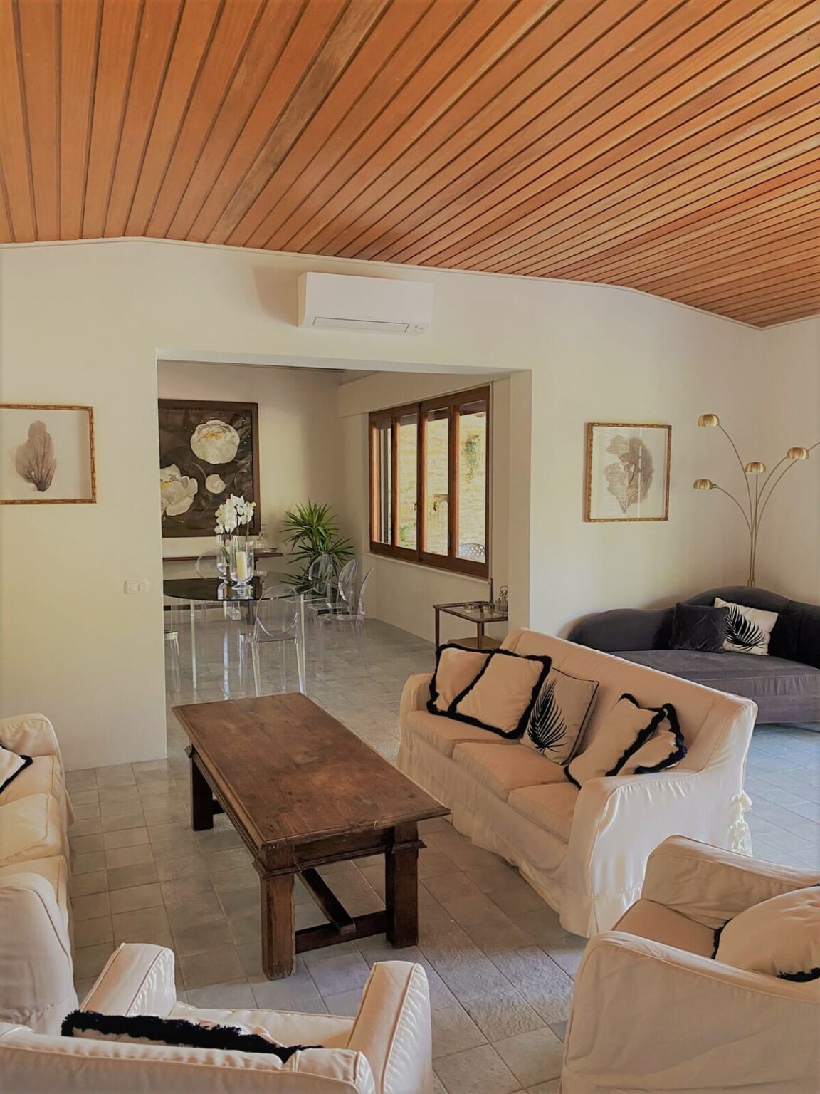Modern living room featuring a cozy sofa, a wooden coffee table, and decorative artwork on the walls. Large windows provide natural light, complemented by indoor plants for a fresh ambiance. | Only on SopranoVillas