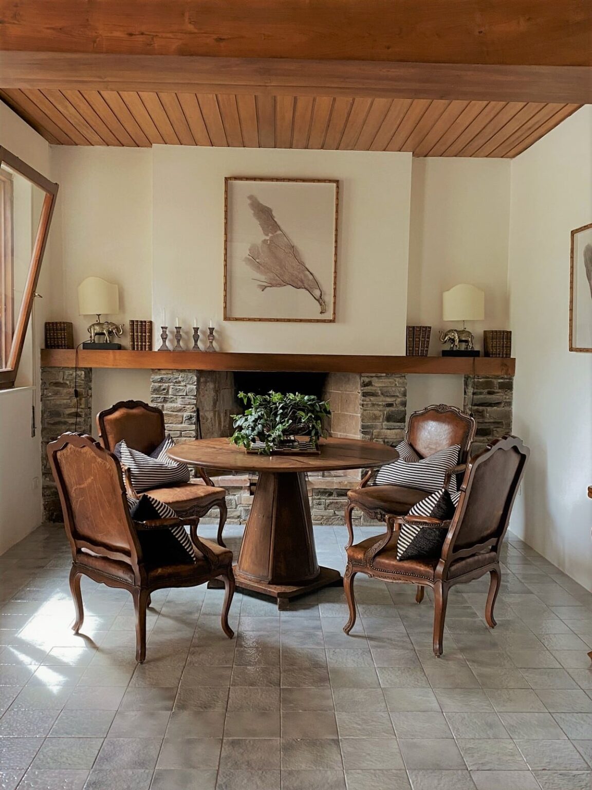 Cozy living room featuring a round wooden table surrounded by two vintage leather chairs, a stone fireplace, and decorative wall art, creating a warm and inviting atmosphere. | Only on SopranoVillas