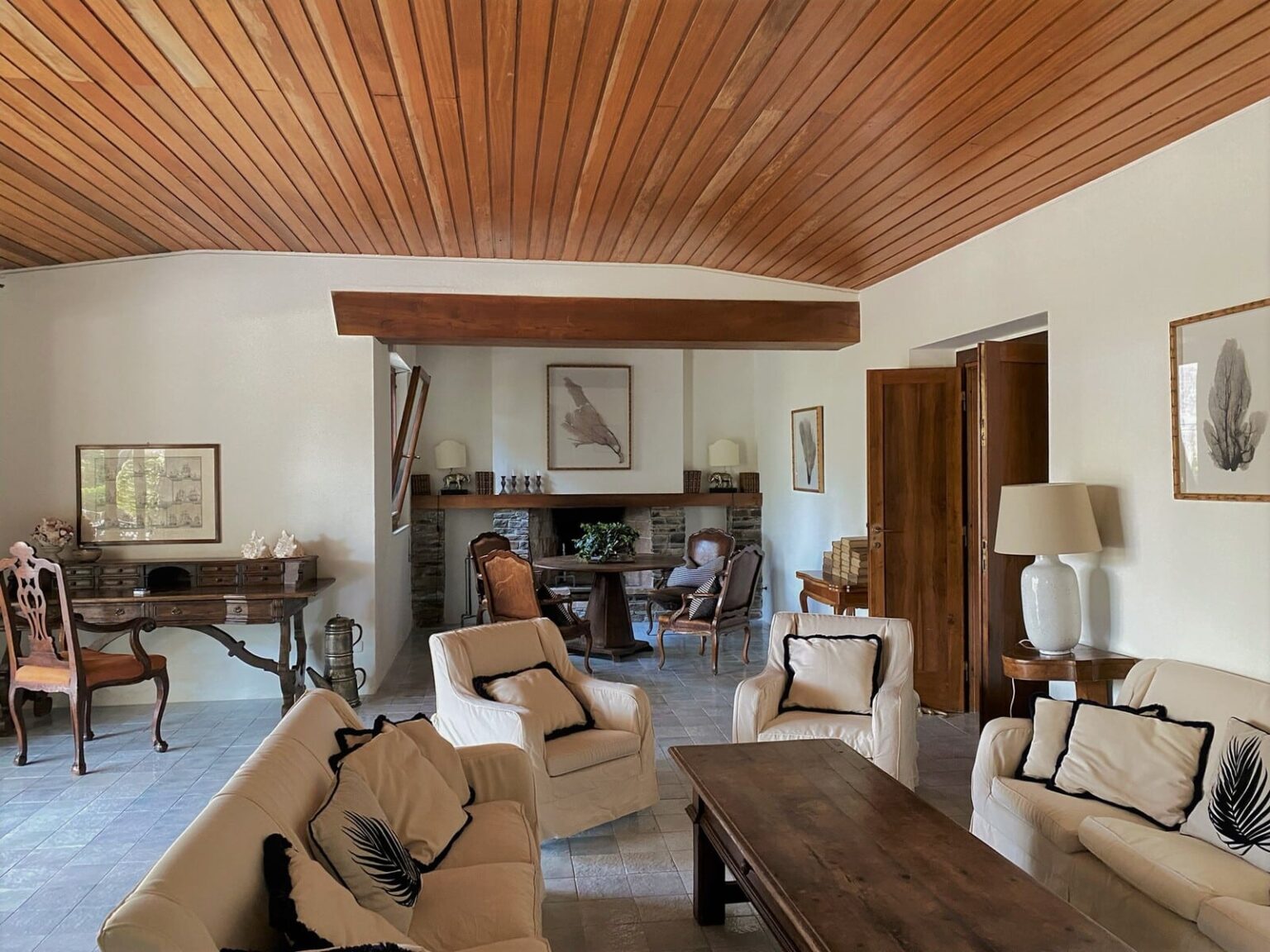 Cozy living room with wooden ceiling, featuring beige upholstered sofas, a wooden coffee table, and a dining area in the background. The space is decorated with framed artwork and has a warm, inviting atmosphere. | Only on SopranoVillas