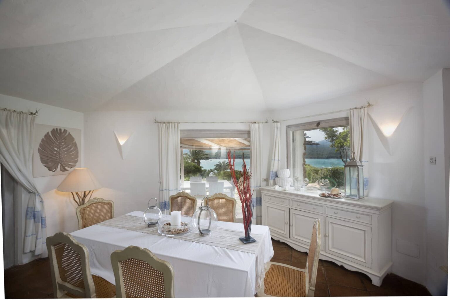 Bright and airy dining room with a white table set for a meal, elegant chairs, and large windows showcasing a scenic view. The room features soft lighting, decorative curtains, and a stylish sideboard, creating a welcoming atmosphere for dining. | Only on SopranoVillas