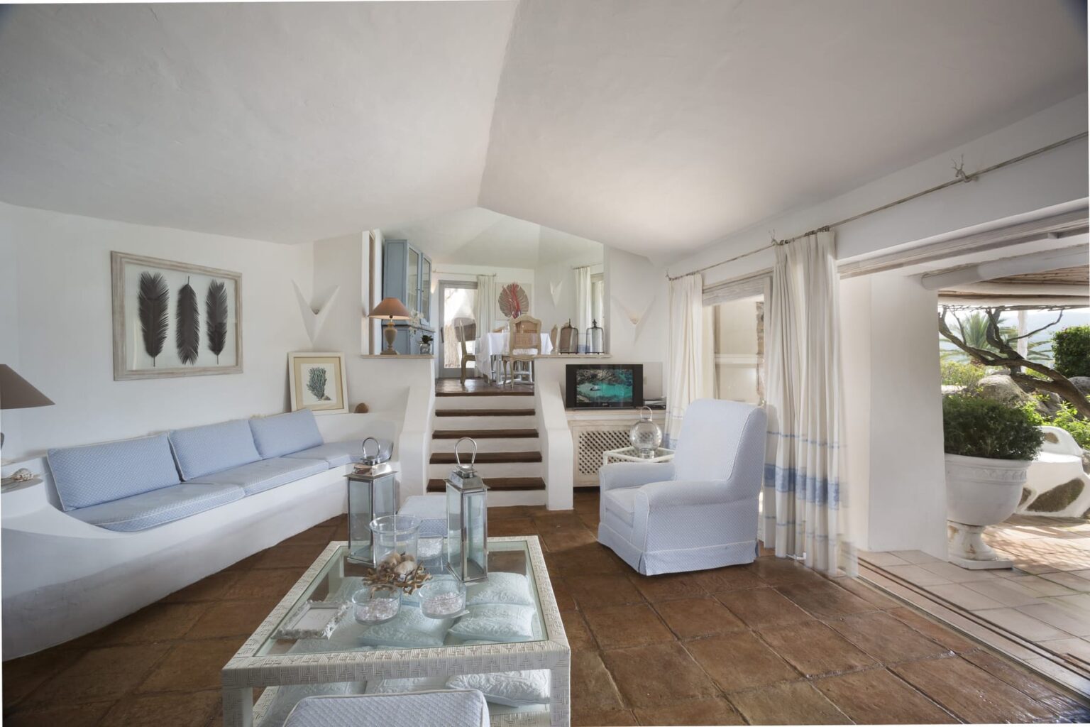 Bright and airy living room featuring a white sofa, stylish decor, and large windows that open to a scenic outdoor space. The room is designed with a modern aesthetic, showcasing natural light and a welcoming atmosphere. | Only on SopranoVillas