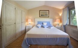 Cozy bedroom featuring a king-sized bed with blue and white bedding, two bedside lamps, and large windows allowing natural light. The room includes a spacious wardrobe and a serene color palette, creating a relaxing atmosphere.