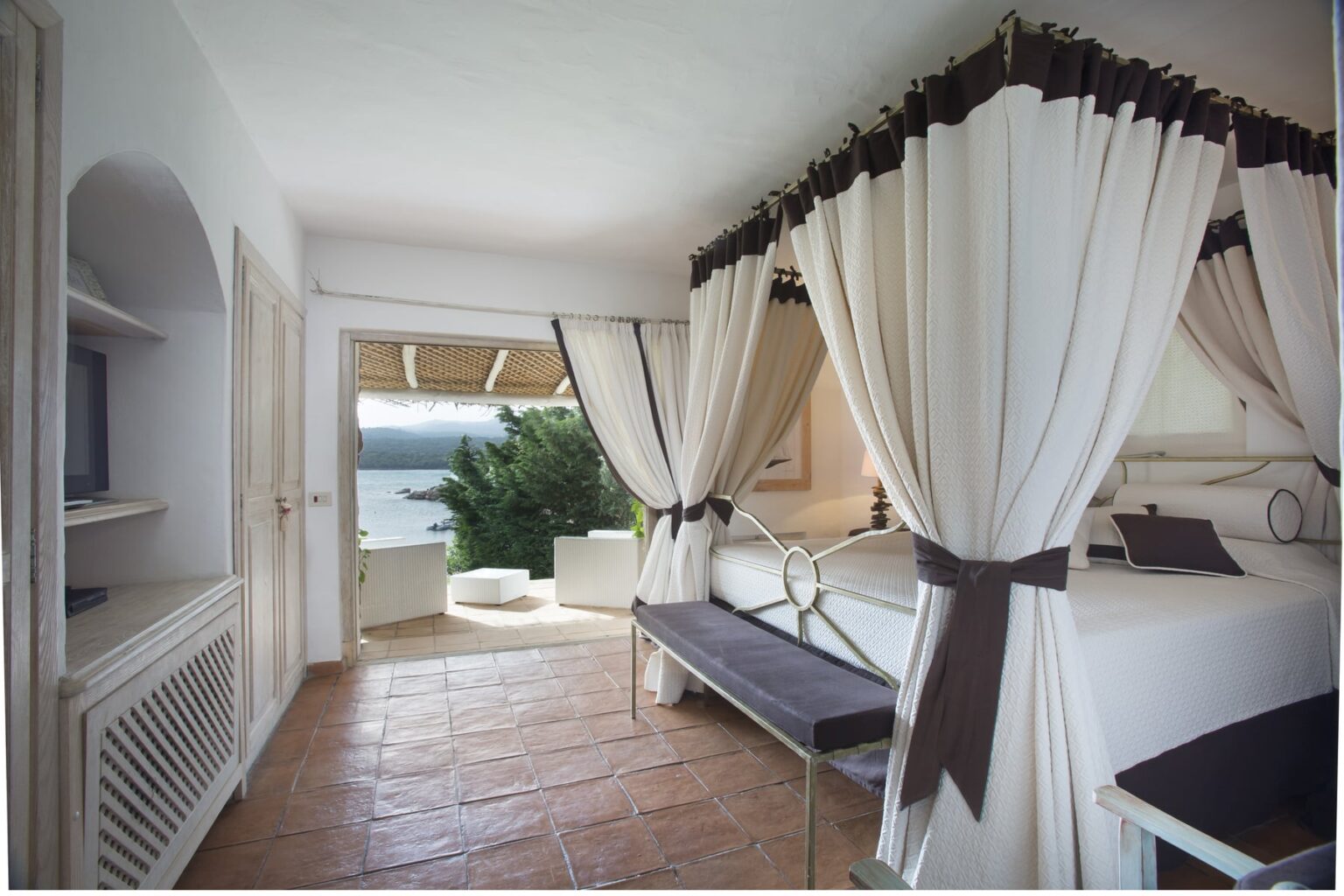 Spacious and elegant hotel room with white drapes, a comfortable bed, and a scenic view of the outdoors, featuring a terrace and natural light streaming in. Ideal for a relaxing getaway. | Only on SopranoVillas