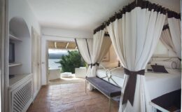 Spacious and elegant hotel room with white drapes, a comfortable bed, and a scenic view of the outdoors, featuring a terrace and natural light streaming in. Ideal for a relaxing getaway.