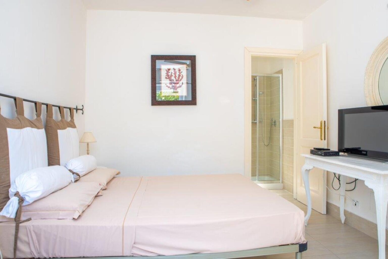 Cozy hotel room featuring a double bed with neutral bedding, a wall-mounted TV, and an en-suite bathroom. Decorated with a framed artwork, the space offers a bright and inviting atmosphere. Ideal for travelers seeking comfort and convenience. | Only on SopranoVillas
