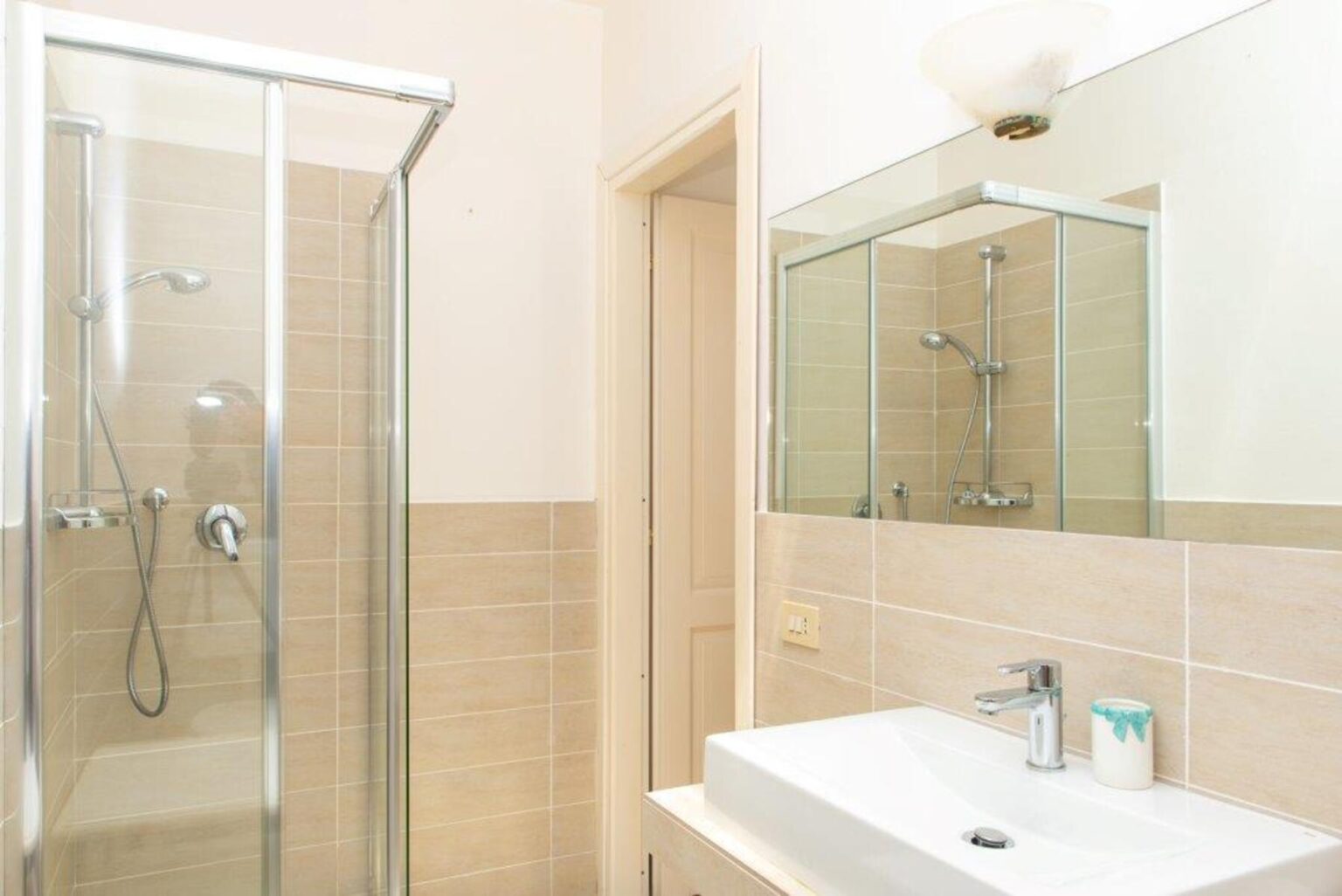 Modern bathroom featuring a glass shower enclosure, sleek sink with a contemporary faucet, and a large mirror. Neutral-toned tiles create a clean and inviting space. | Only on SopranoVillas