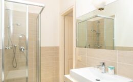 Modern bathroom featuring a glass shower enclosure, sleek sink with a contemporary faucet, and a large mirror. Neutral-toned tiles create a clean and inviting space.