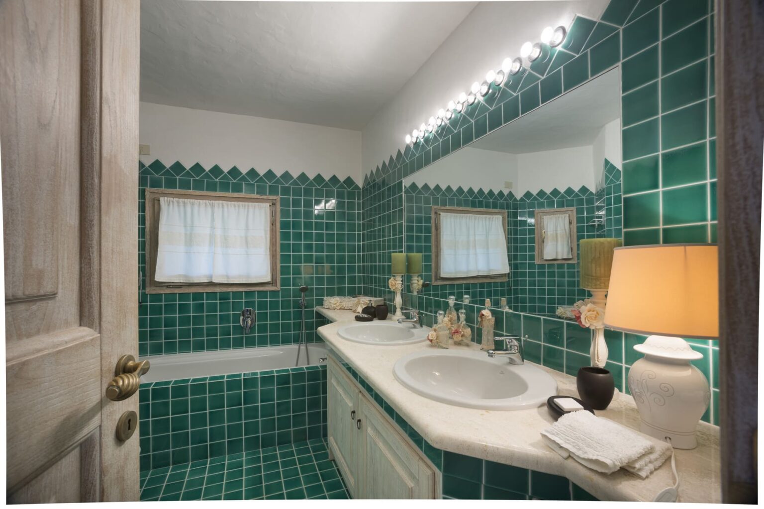 Brightly lit bathroom featuring vibrant green tiled walls and floor, a white countertop with sink, and a decorative lamp, creating a stylish and inviting space. | Only on SopranoVillas