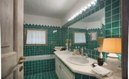 Brightly lit bathroom featuring vibrant green tiled walls and floor, a white countertop with sink, and a decorative lamp, creating a stylish and inviting space.