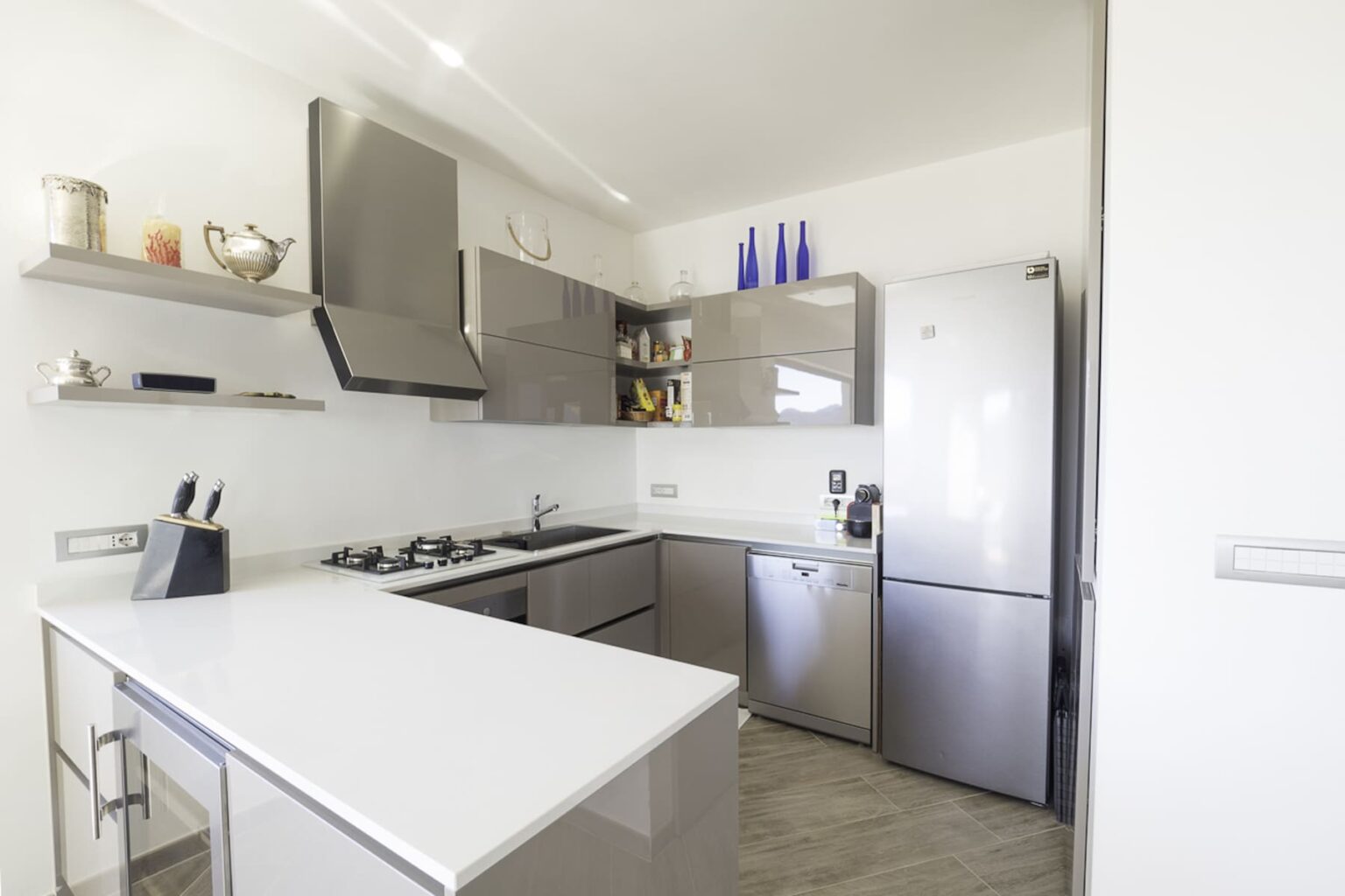 Modern kitchen featuring stainless steel appliances, including a refrigerator and gas stove, with sleek cabinetry and white countertops, designed for efficiency and style. | Only on SopranoVillas