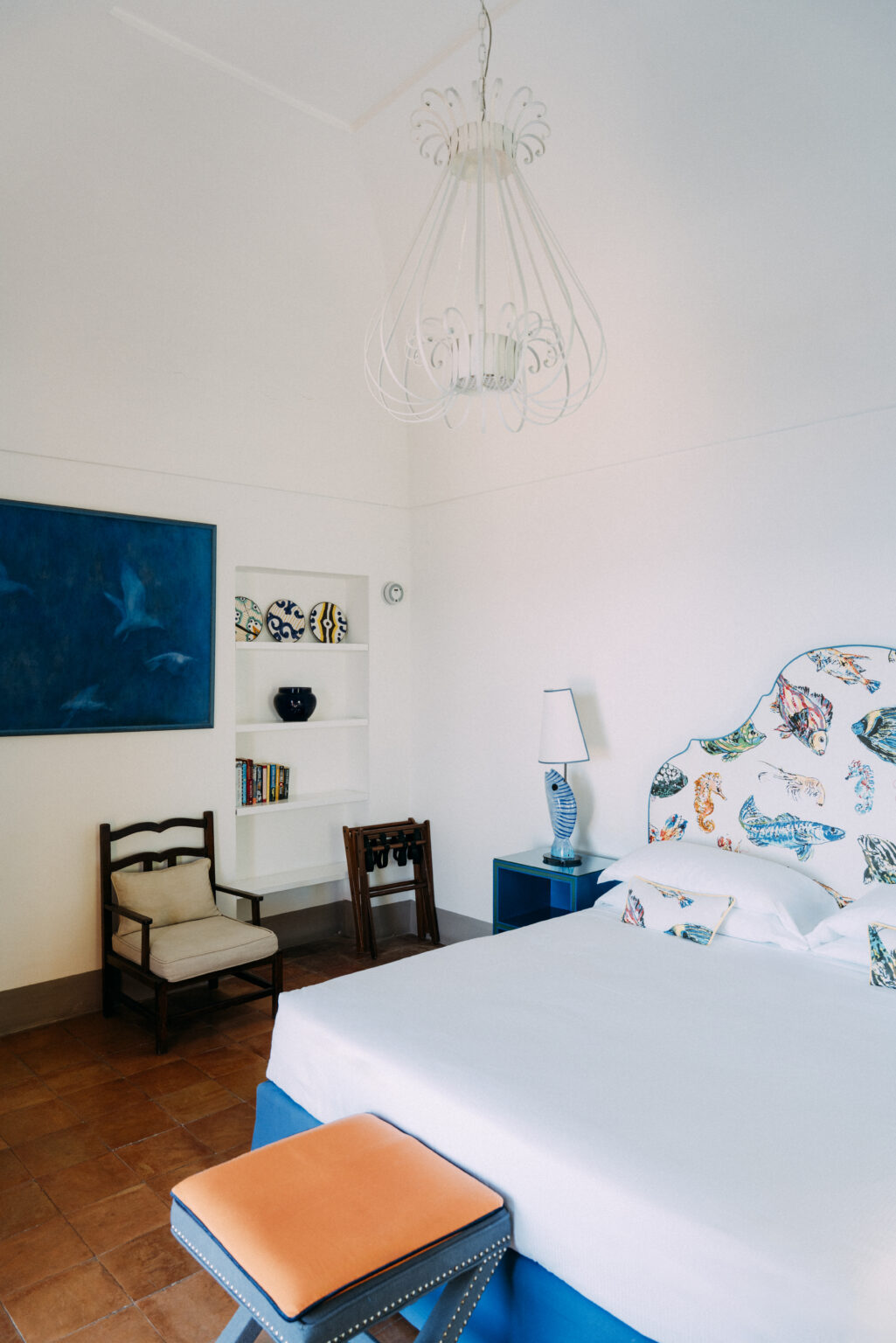 Bright and airy bedroom featuring a colorful upholstered headboard, a blue accent table, and decorative wall art. The room includes a bookshelf with decorative items and a stylish lamp, creating a modern and inviting atmosphere. | Only on SopranoVillas