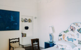 Bright and airy bedroom featuring a colorful upholstered headboard, a blue accent table, and decorative wall art. The room includes a bookshelf with decorative items and a stylish lamp, creating a modern and inviting atmosphere.