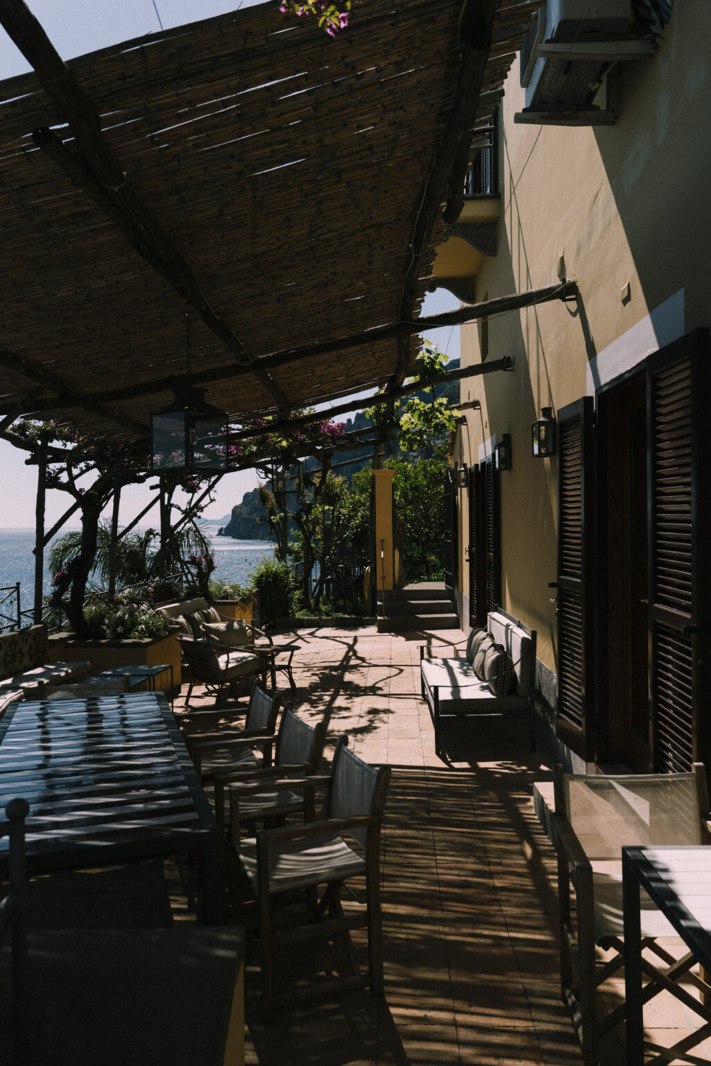Cozy outdoor terrace with seating overlooking the ocean, featuring lush greenery and a scenic coastal view. Ideal for relaxation and dining in a tranquil setting. | Only on SopranoVillas