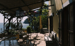 Cozy outdoor terrace with seating overlooking the ocean, featuring lush greenery and a scenic coastal view. Ideal for relaxation and dining in a tranquil setting.