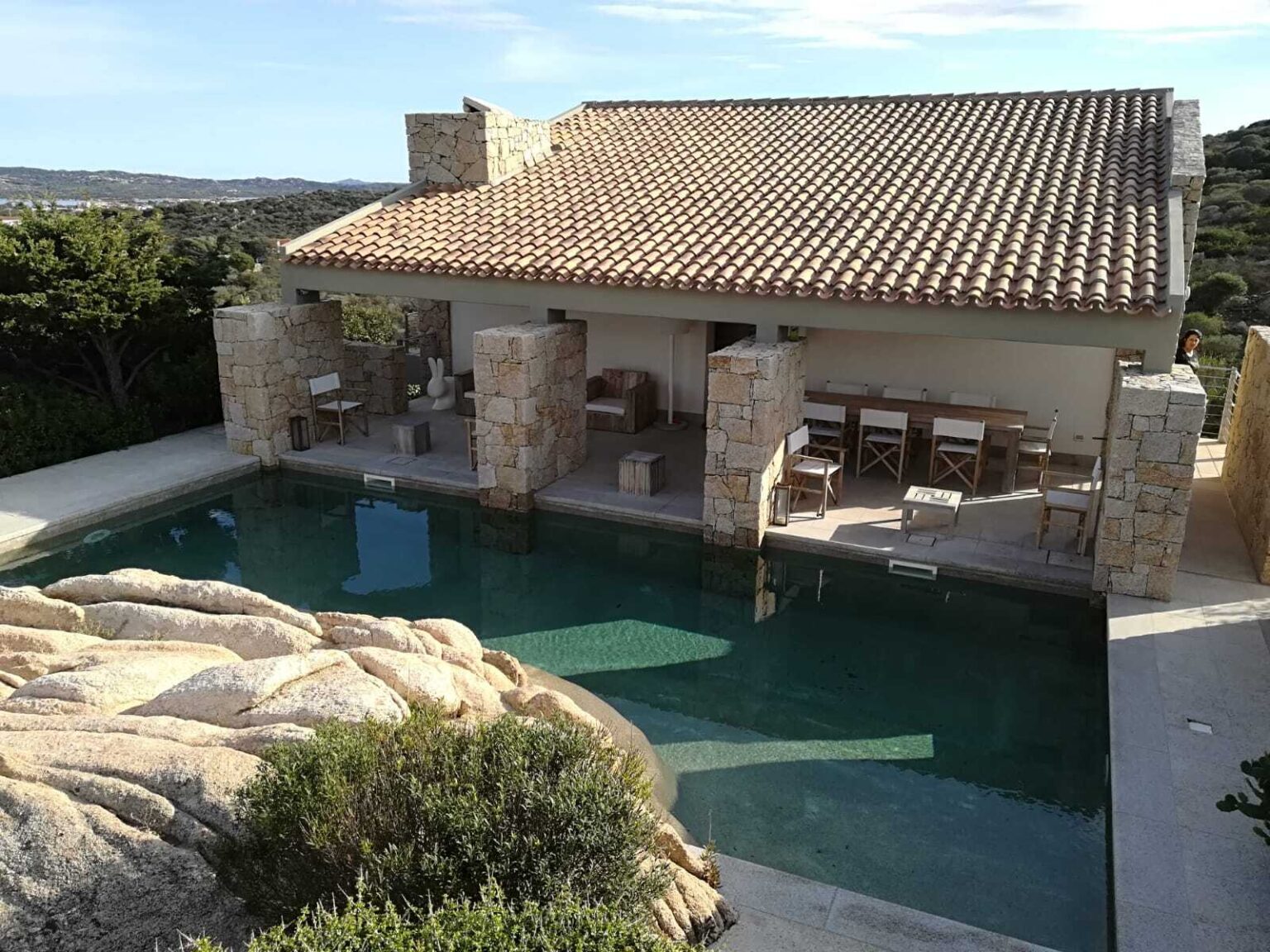 Modern villa with a stone exterior and a private pool, surrounded by lush greenery. The outdoor area features a patio with seating, offering a serene retreat. | Only on SopranoVillas