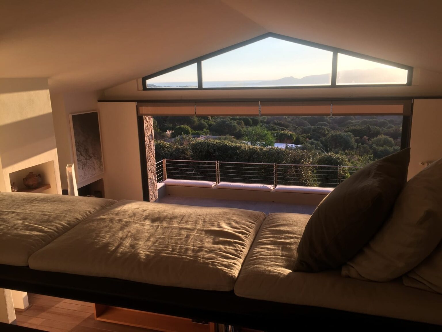 Cozy loft space with a large window offering a panoramic view of lush greenery and distant mountains, featuring a comfortable, cushioned seating area. | Only on SopranoVillas