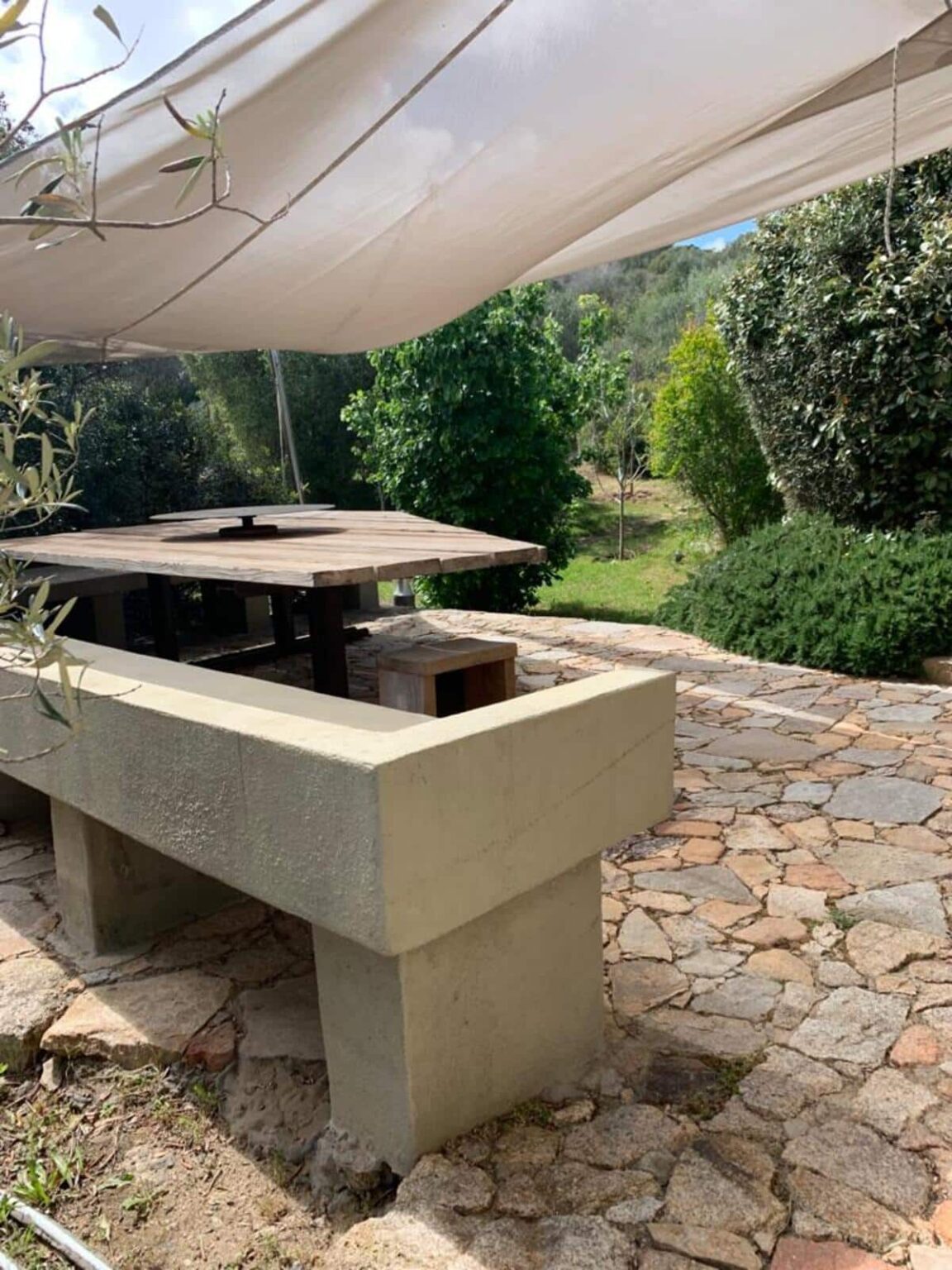 Outdoor dining area featuring a wooden table and stone pathway, surrounded by greenery and trees, ideal for relaxation and gatherings. | Only on SopranoVillas