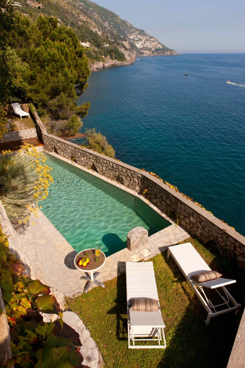 Luxury villa rental in Italy featuring an elegant infinity pool overlooking a serene lake, surrounded by lush greenery and stone walls for privacy. Perfect for a tranquil getaway. | Only on SopranoVillas