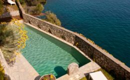 Luxury villa rental in Italy featuring an elegant infinity pool overlooking a serene lake, surrounded by lush greenery and stone walls for privacy. Perfect for a tranquil getaway.