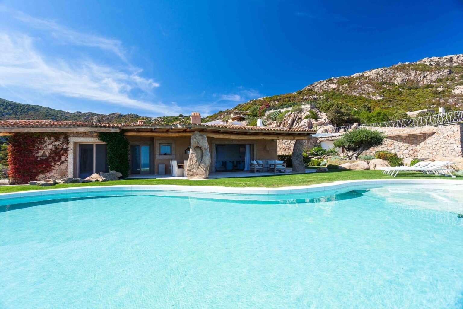 Luxury villa with a swimming pool, surrounded by lush greenery and mountains under a clear blue sky. Ideal for a relaxing getaway or vacation rental. | Only on SopranoVillas