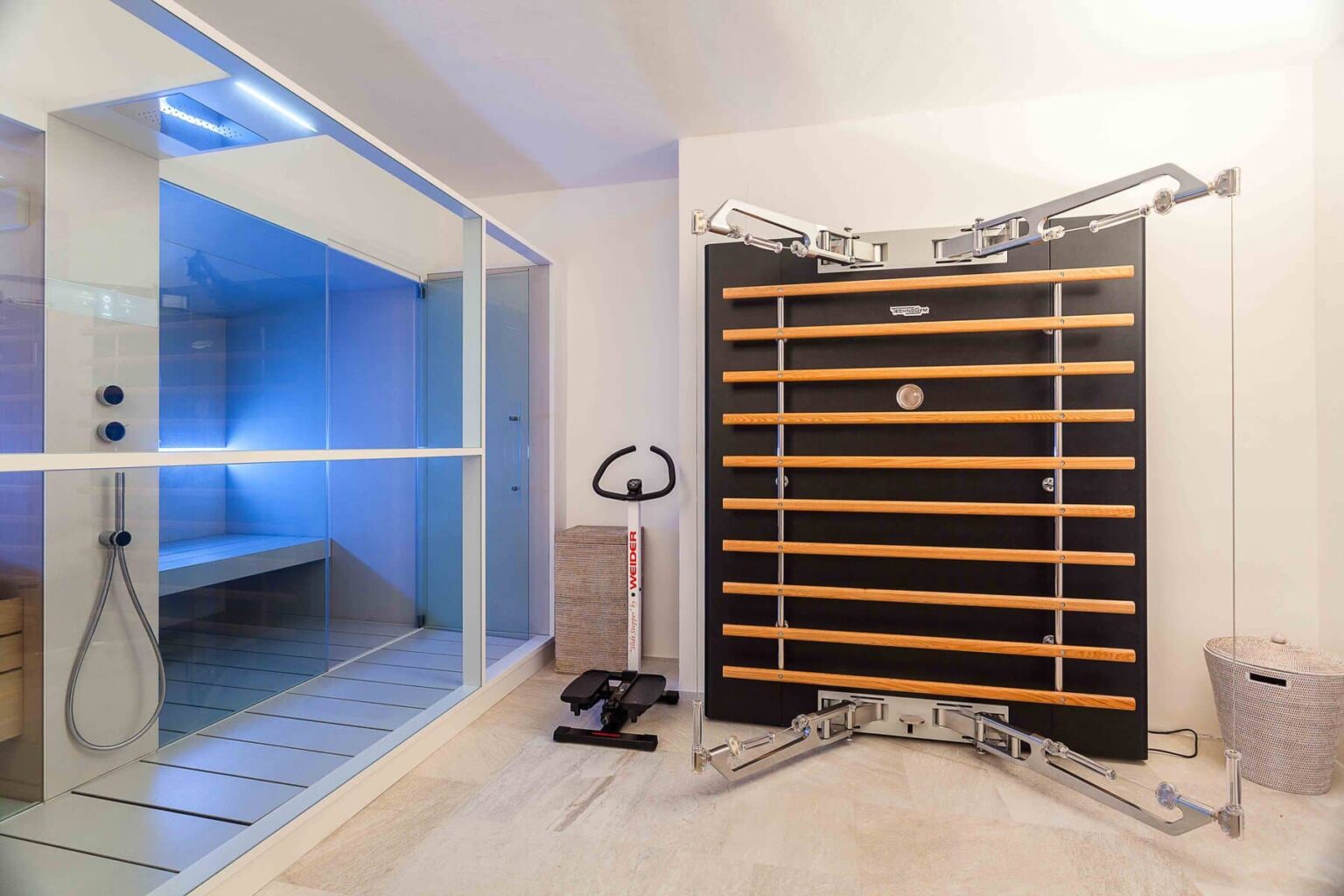 Modern home gym featuring a wooden wall-mounted exercise station and a glass-enclosed sauna with blue lighting, promoting fitness and relaxation. | Only on SopranoVillas