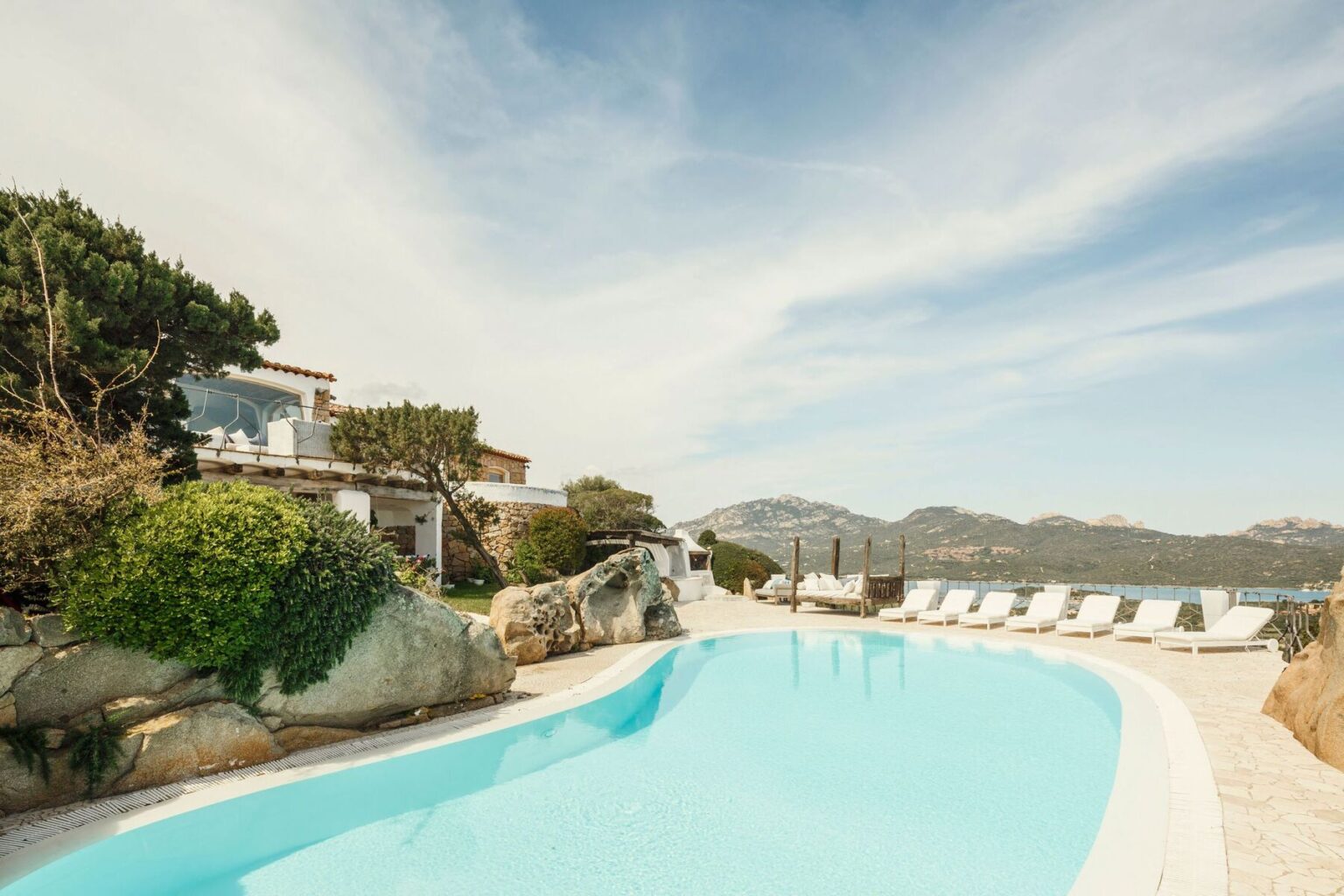 Luxurious villa with a pristine swimming pool, surrounded by lush greenery and rocky landscapes, offering stunning mountain and sea views in a tranquil setting. | Only on SopranoVillas