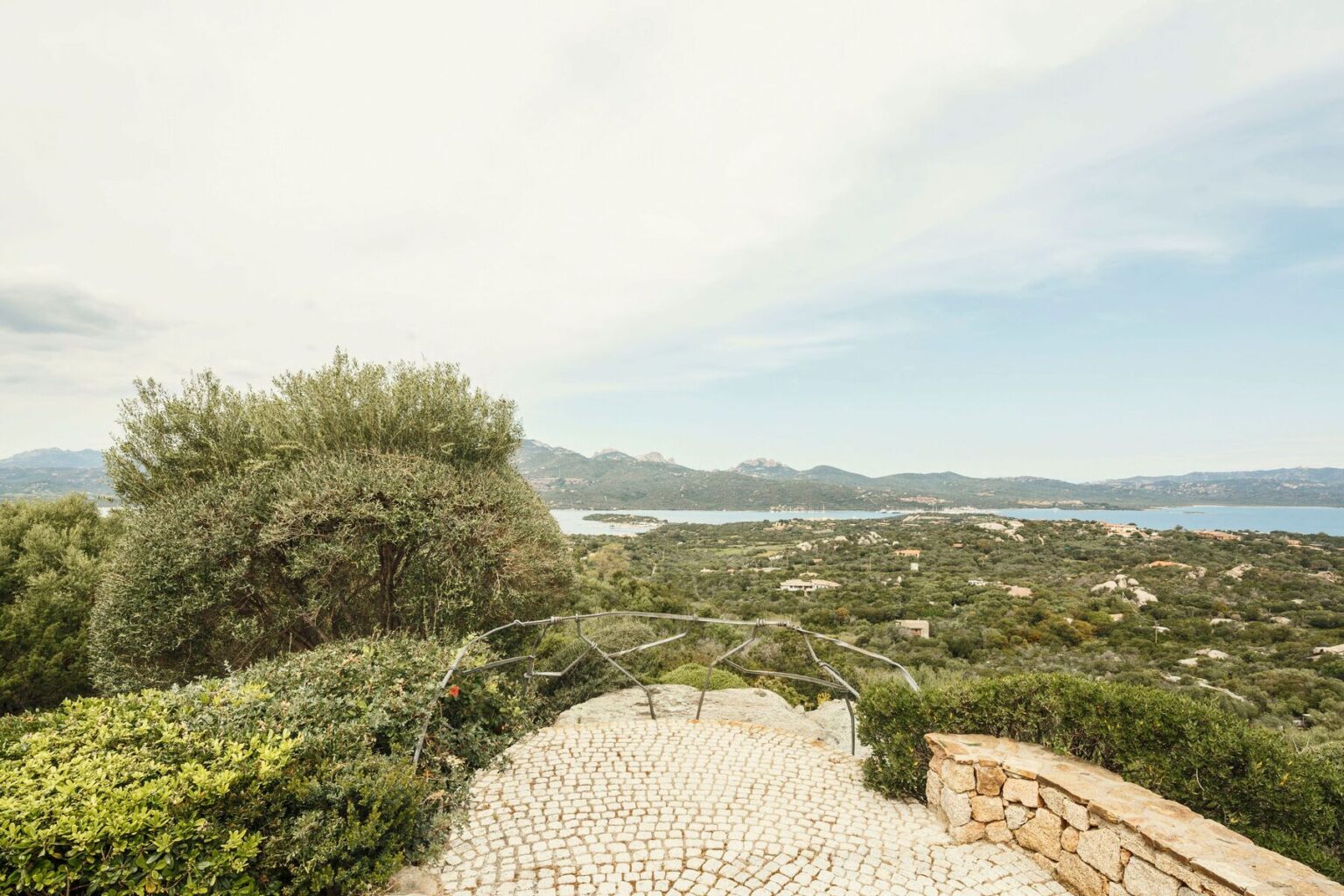 Scenic view of a coastal landscape featuring lush greenery, rolling hills, and a serene body of water under a partly cloudy sky. | Only on SopranoVillas