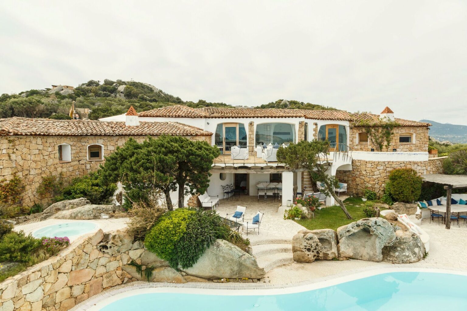 Luxurious stone villa with a spacious terrace, surrounded by lush greenery and rocky landscapes, featuring a swimming pool and scenic mountain views. | Only on SopranoVillas