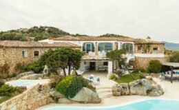 Luxurious stone villa with a spacious terrace, surrounded by lush greenery and rocky landscapes, featuring a swimming pool and scenic mountain views.