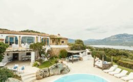 Stunning villa with a pool overlooking scenic hills and water, featuring outdoor seating and lush greenery, ideal for luxury vacations.