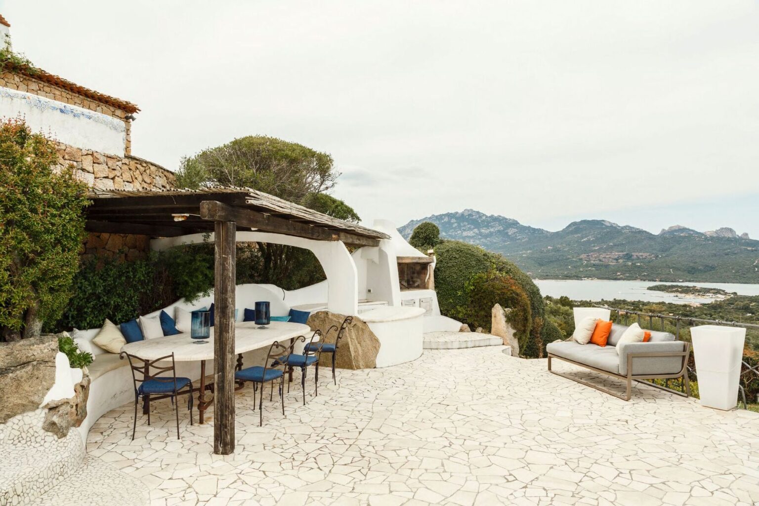 Outdoor patio area with a dining table and chairs, surrounded by lush greenery and mountains in the background, offering a scenic view of the landscape. Ideal for relaxation and entertaining. | Only on SopranoVillas
