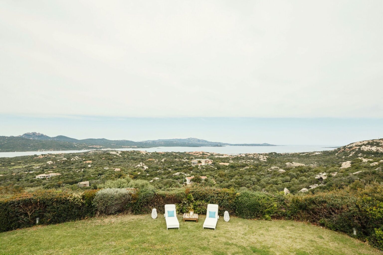 Scenic view of a coastal landscape with two lounge chairs in the foreground, overlooking greenery and a serene ocean in the distance under a cloudy sky. | Only on SopranoVillas