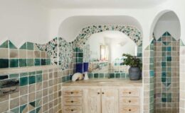 Stylish bathroom featuring patterned green and beige tiles, a wooden vanity with multiple drawers, and an archway design that adds a touch of elegance. Natural light illuminates the space, highlighting the decorative details and a potted plant on the countertop.
