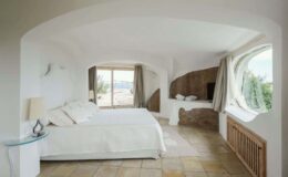 Spacious, modern bedroom with a large window offering scenic views, featuring a comfortable king-size bed, minimalist decor, and natural stone accents.