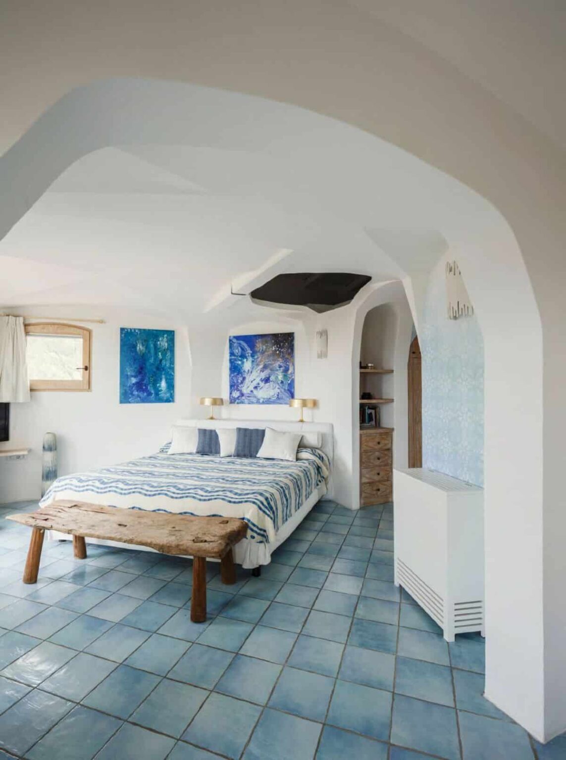 Cozy bedroom featuring a white decor with blue accents, a large bed with patterned bedding, wooden furniture, and abstract wall art, creating a serene and inviting atmosphere. | Only on SopranoVillas