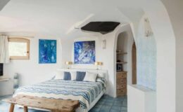 Cozy bedroom featuring a white decor with blue accents, a large bed with patterned bedding, wooden furniture, and abstract wall art, creating a serene and inviting atmosphere.