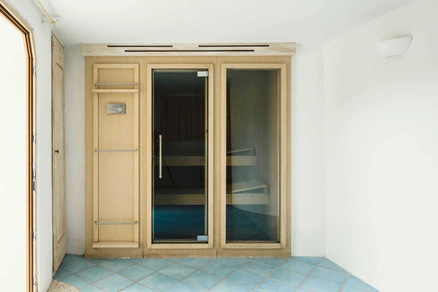 Modern sauna with wooden accents and glass doors, featuring blue tiled flooring and a minimalist design, ideal for relaxation and wellness. | Only on SopranoVillas