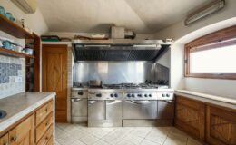 Modern kitchen interior featuring stainless steel appliances, a professional-grade cooking range, and wooden cabinetry. The space is well-lit with natural light from a window, showcasing a clean and functional design.